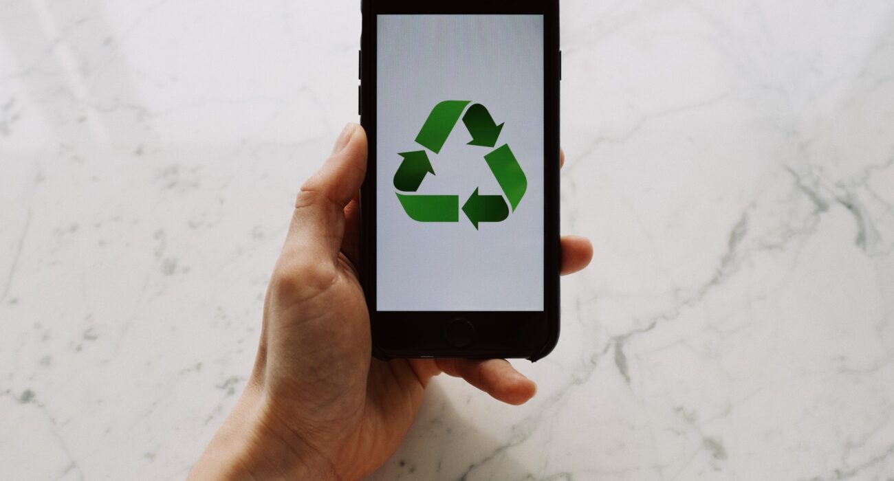 From above view of faceless person holding mobile phone with white screen and green recycle logo above marble surface