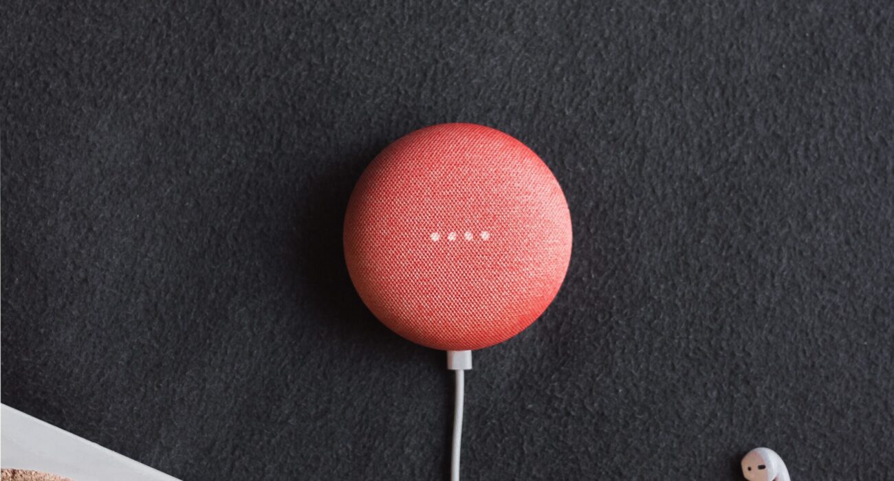 flat lay photography of coral Google Home Mini on black surface beside Apple AirPods
